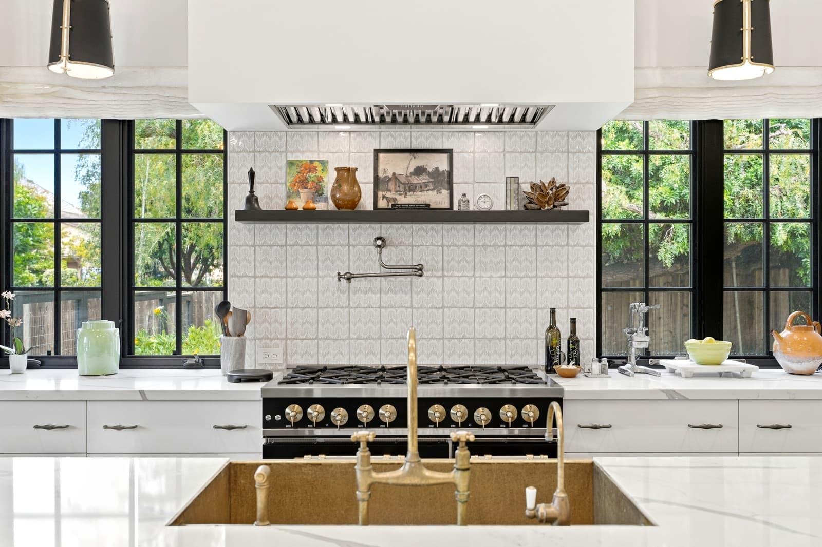 Kitchen with a brass farmhouse sink and a black range between steel windows, seen straight on