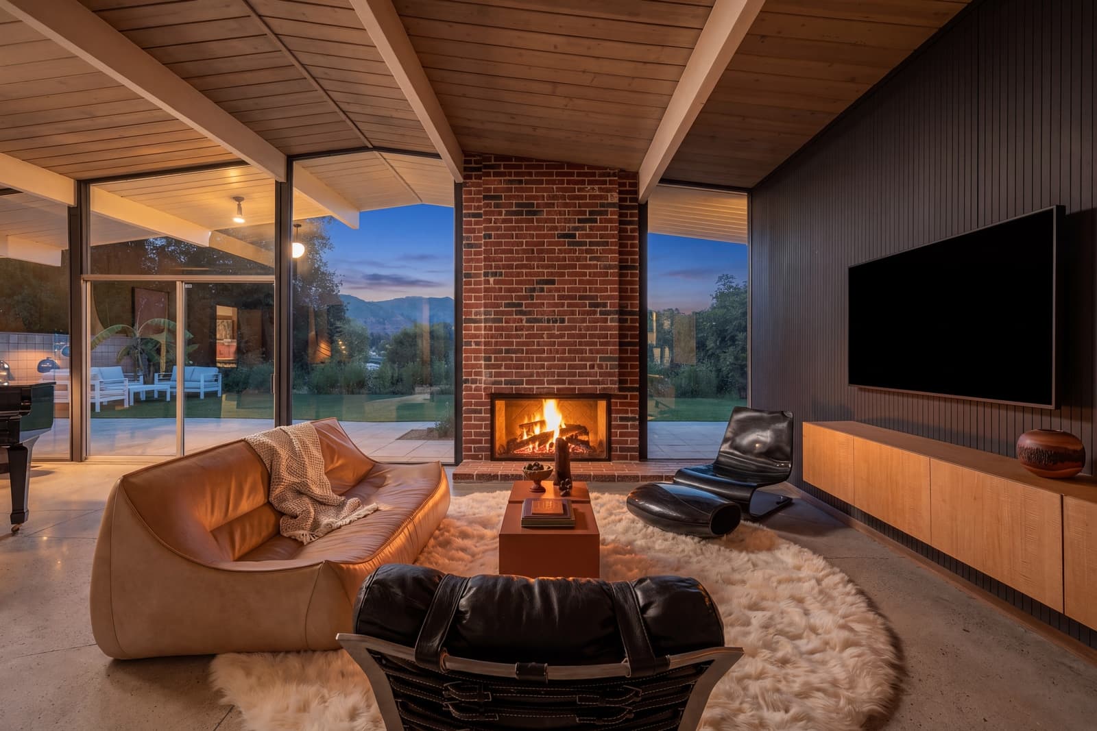 Brick fireplace lit at dusk, glass walls open to the sky on both sides
