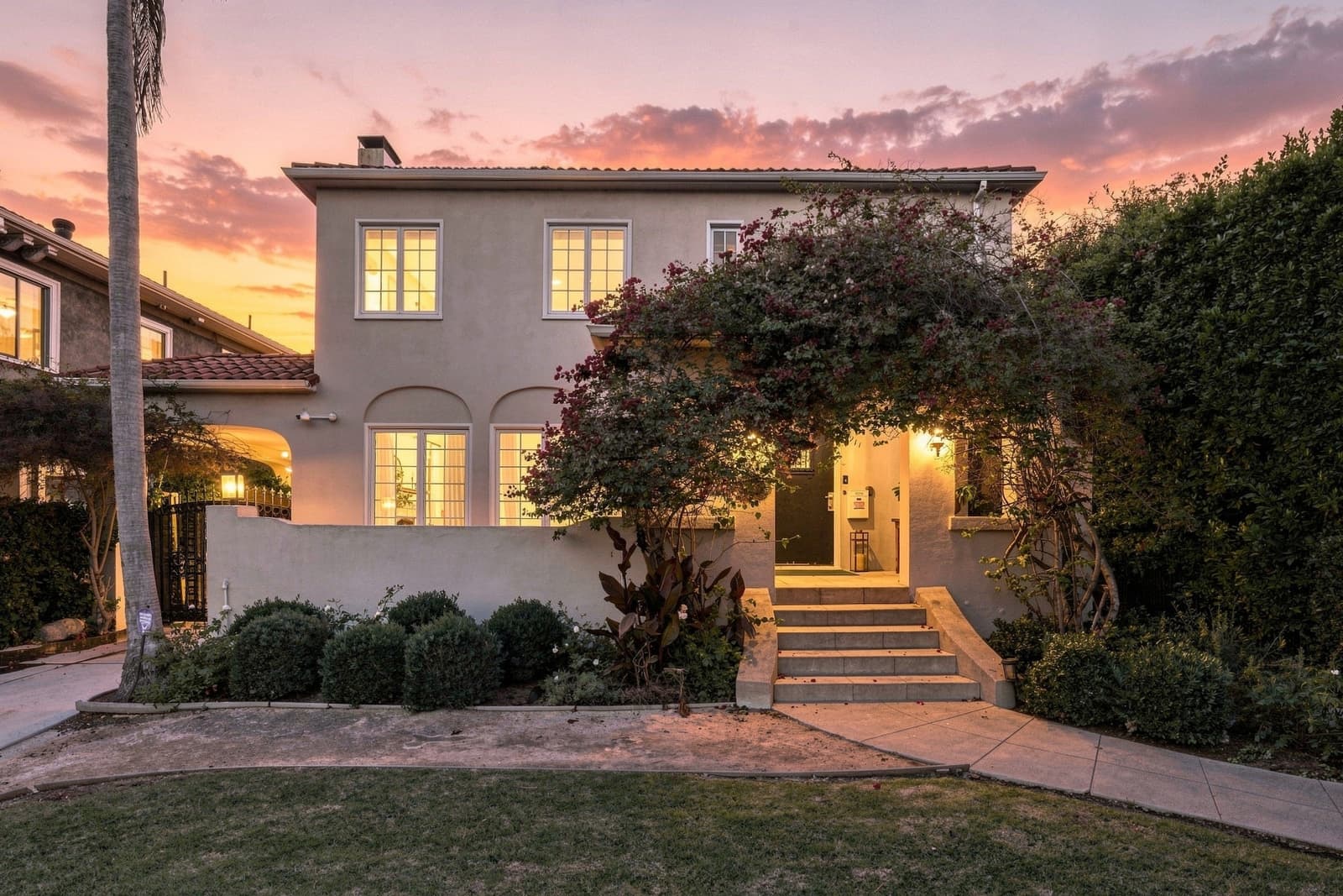 Spanish two-story at twilight, bougainvillea over the lit arched door